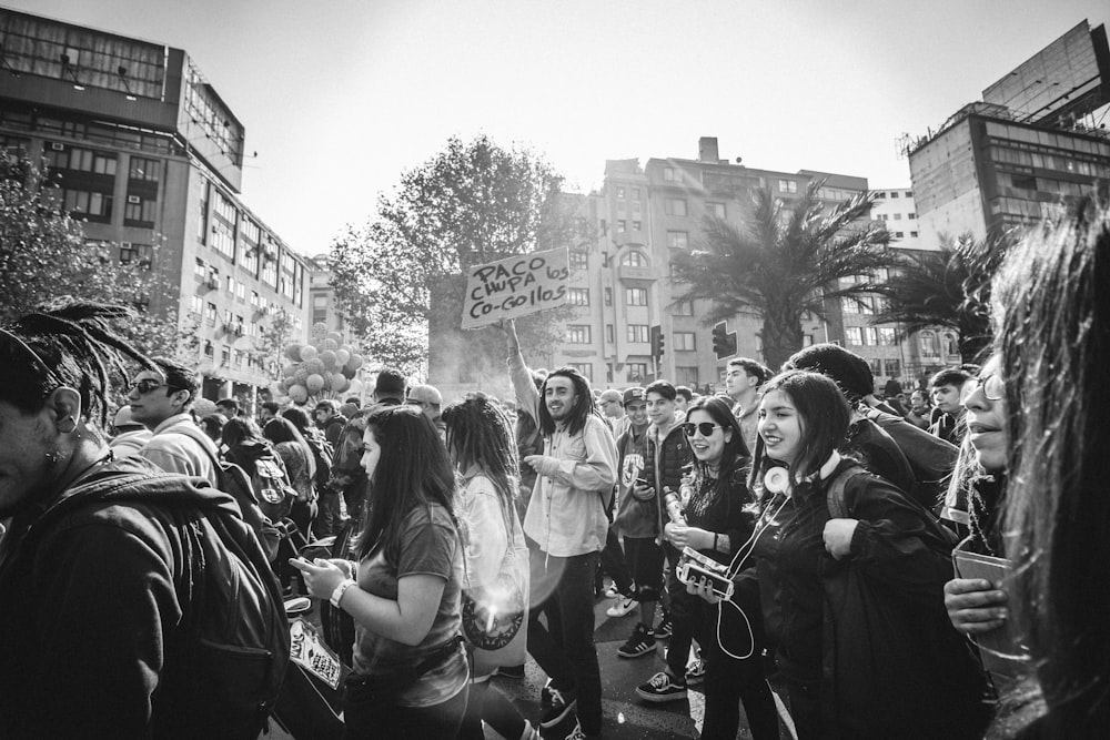 grayscale photography of group of people on street near high-rise buildings