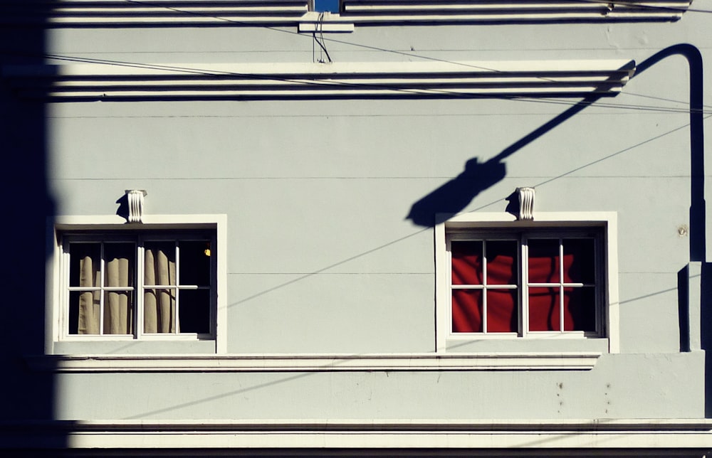 Weißes Hausfenster mit rotem Vorhang und Schatten des Straßenpfostens während des Tages