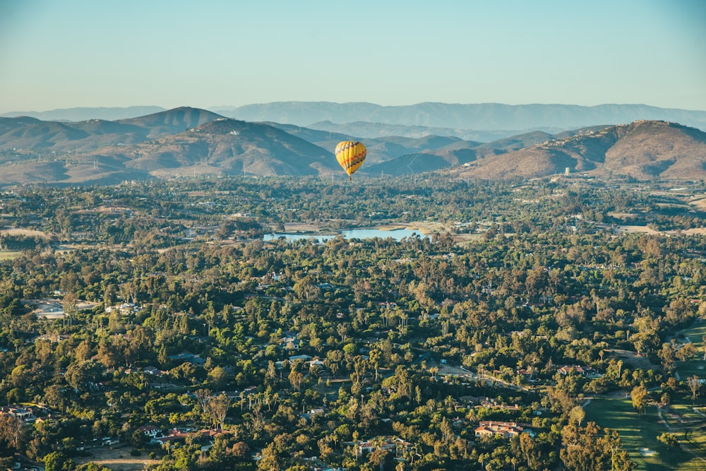 yellow hot air balloon with green trees under