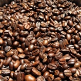 A close-up view of numerous roasted coffee beans, with a rich and glossy appearance, highlighting their textures and deep brown colors.
