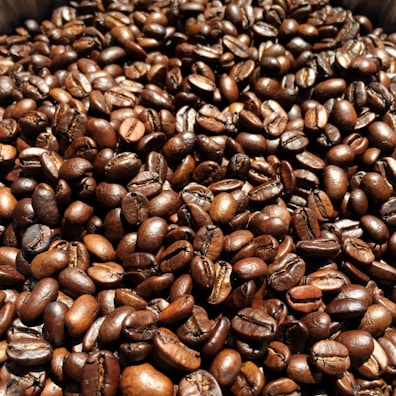 A close-up view of numerous roasted coffee beans, with a rich and glossy appearance, highlighting their textures and deep brown colors.