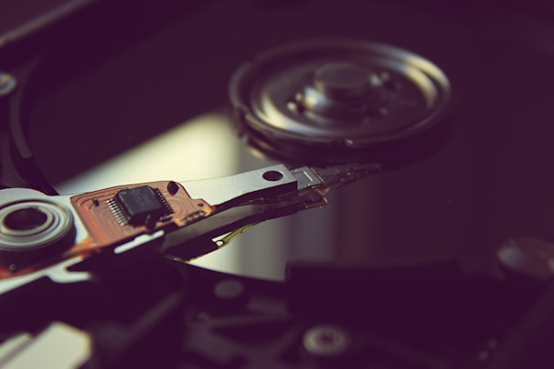 A close-up view of the internal components of a hard disk drive, including the read/write head and platter. The intricate details of the electronic circuit board and metallic components are visible, with a focus on the mechanical parts.