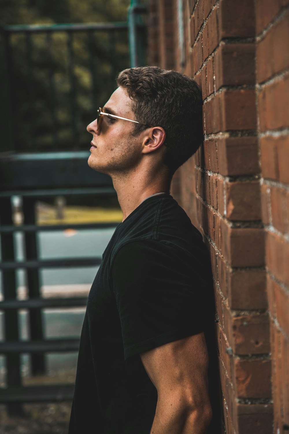 man in black short-sleeved shirt leaning on brow brick wall