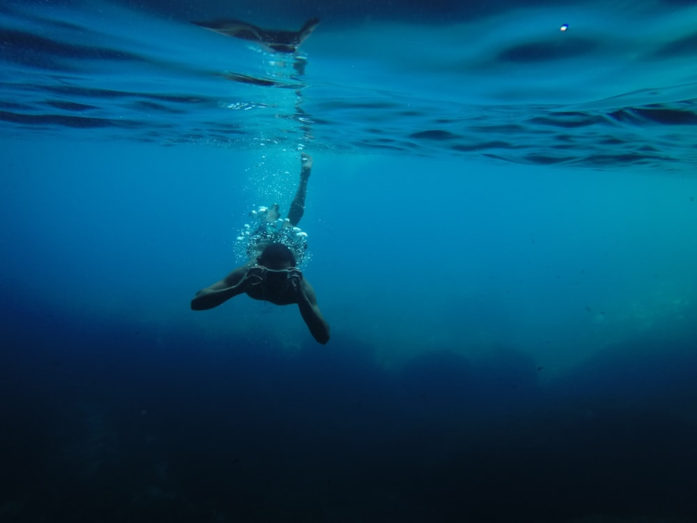 Persona que usa gafas protectoras mientras nada bajo el cuerpo de agua