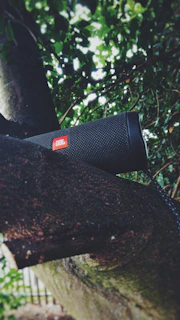 A sleek portable speaker resting on a wooden picnic table with sunlight filtering through leaves.