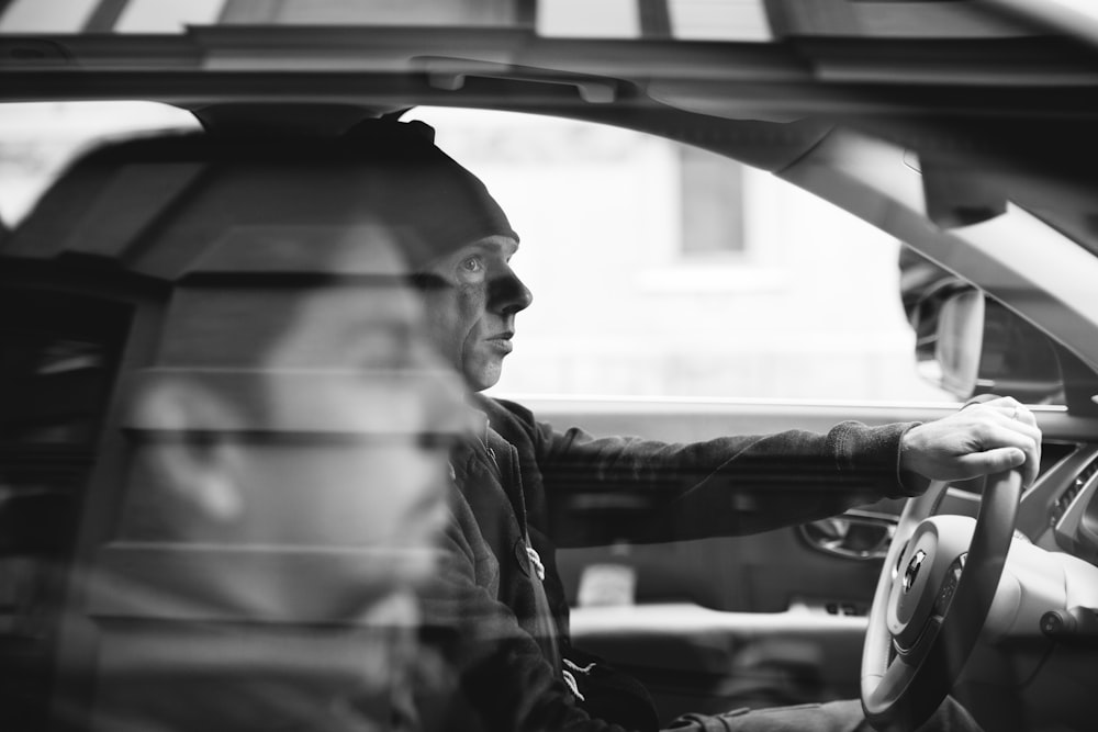 grayscale photo of two men riding on vehicle