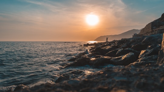 person standing on rock facing ocean during golden hour in Cinque Terre National Park Italy
