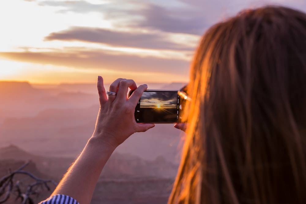 Mujer tomando foto de la puesta de sol naranja