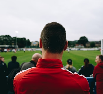 man standing while watching soccer during daytime