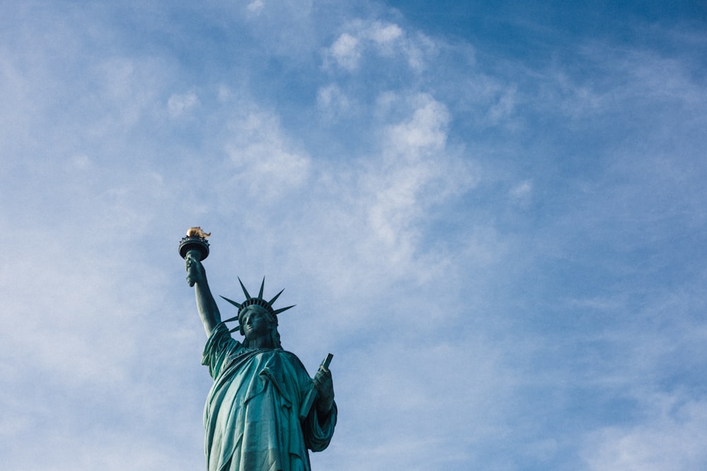 photo en contre-plongée de la Statue de la Liberté sous un ciel nuageux bleu et blanc