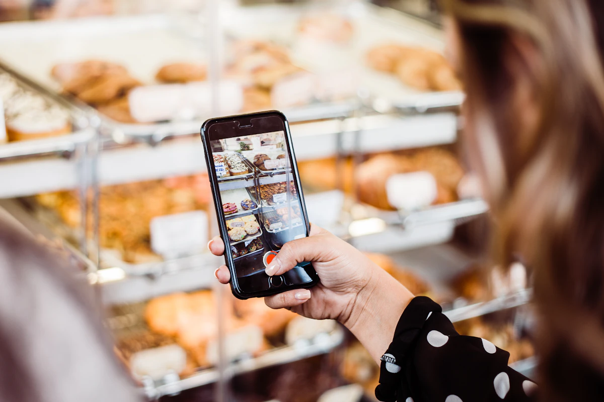 Une personne photographie avec son smartphone une vitrine remplie de viennoiseries dans une boulangerie