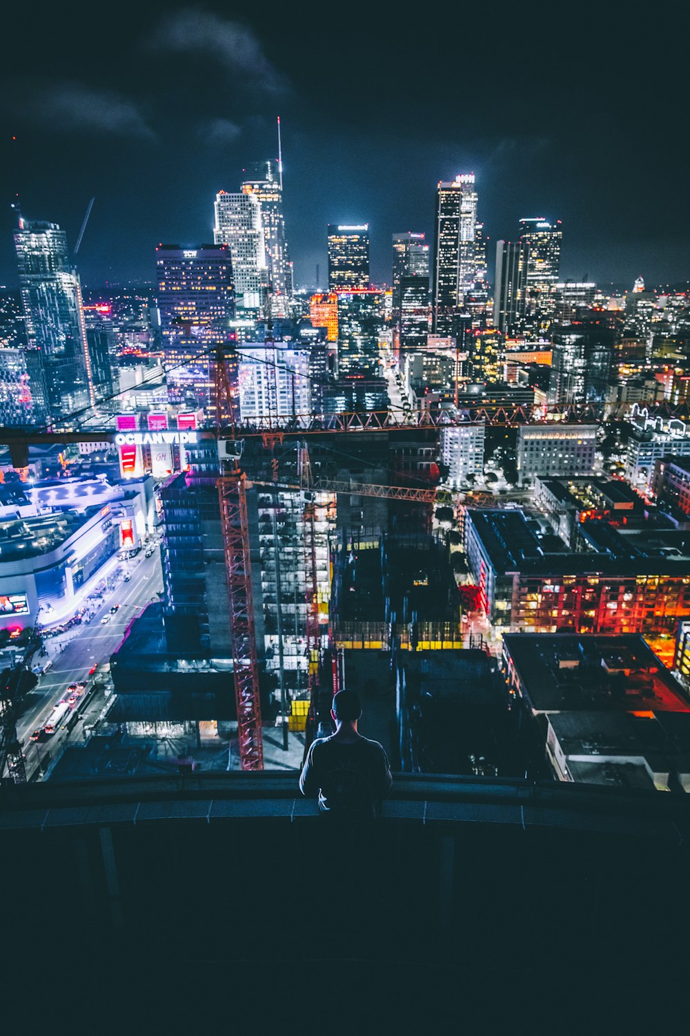 man sitting on building ledge facing skyscraper