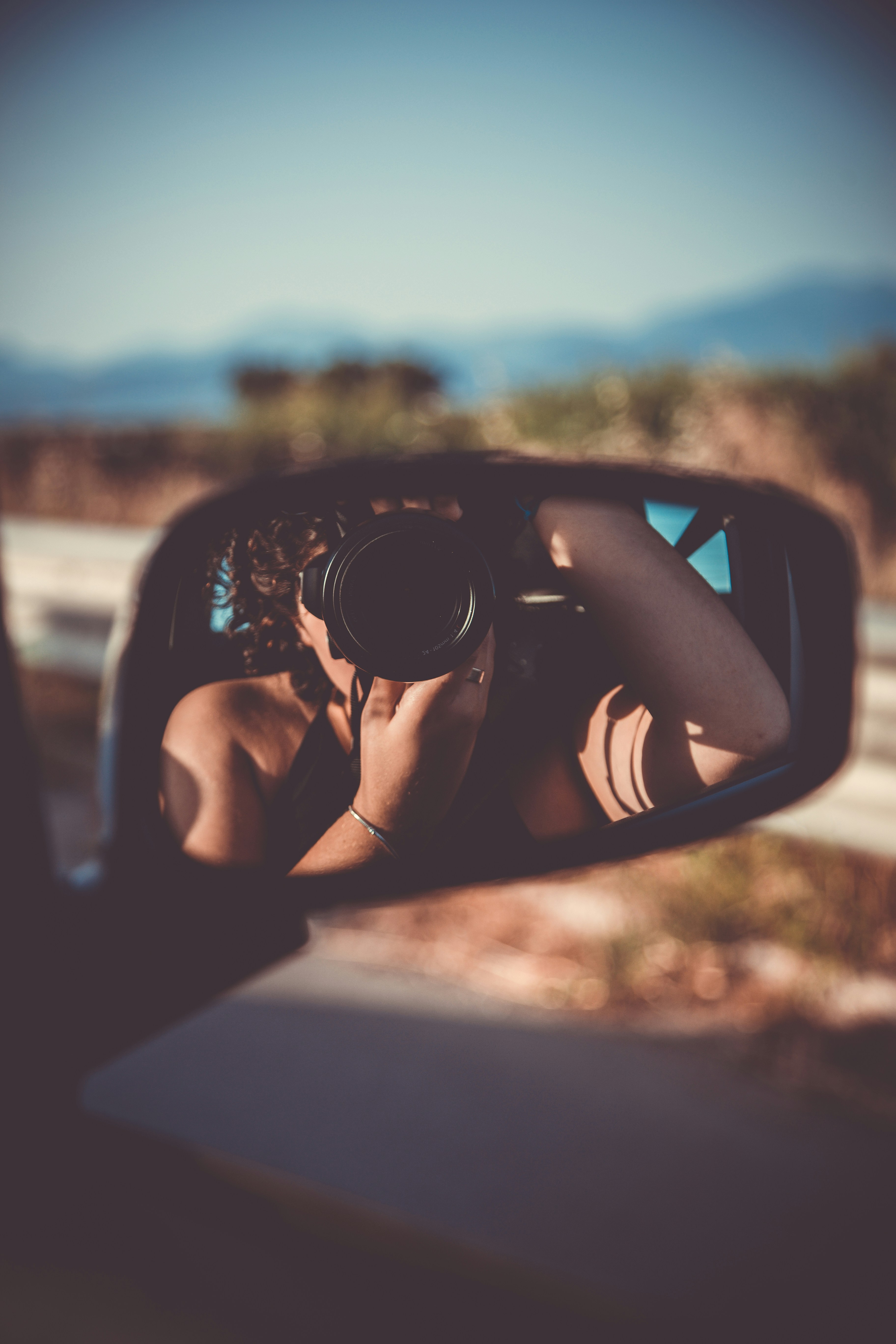 Photographer with camera with a big lens takes self-portrait in car’s wing mirror