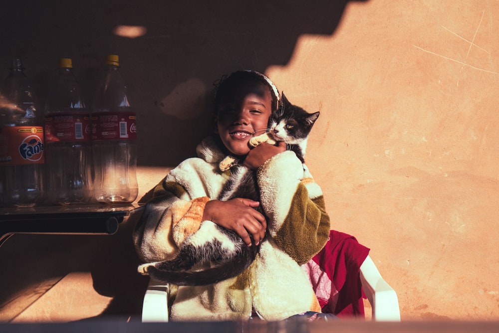 menina sorridente abraçando gato encostado na parede