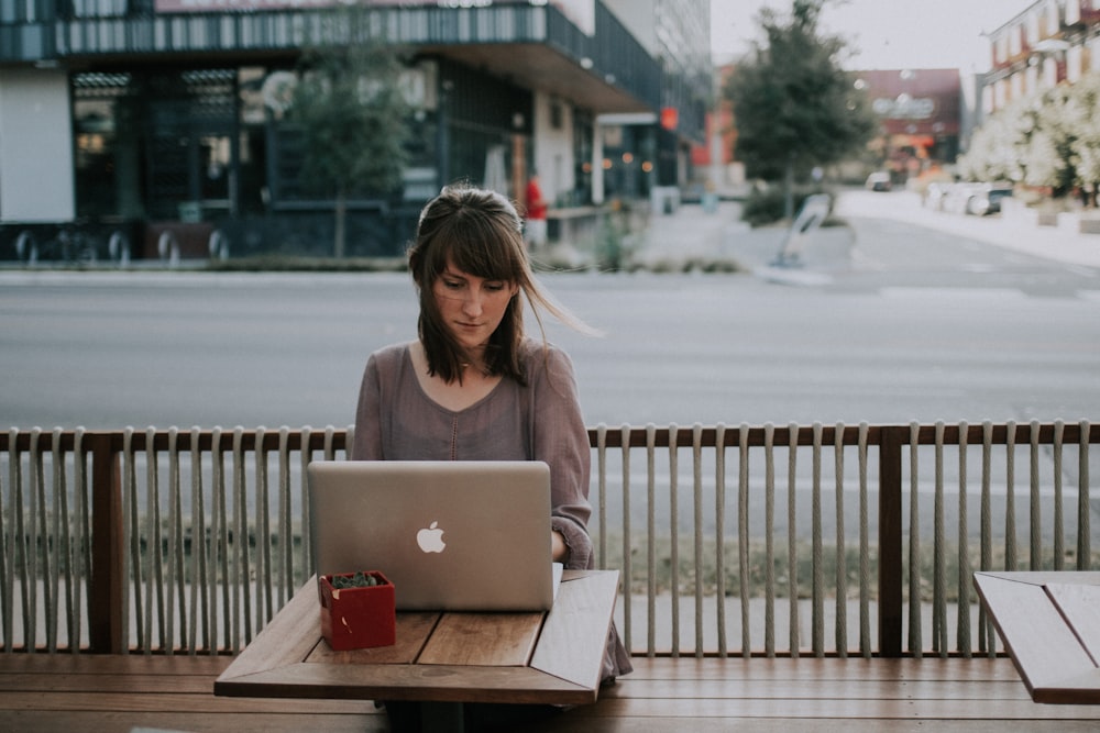 MacBookの前のベンチに座っているグレーのシャツを着た女性