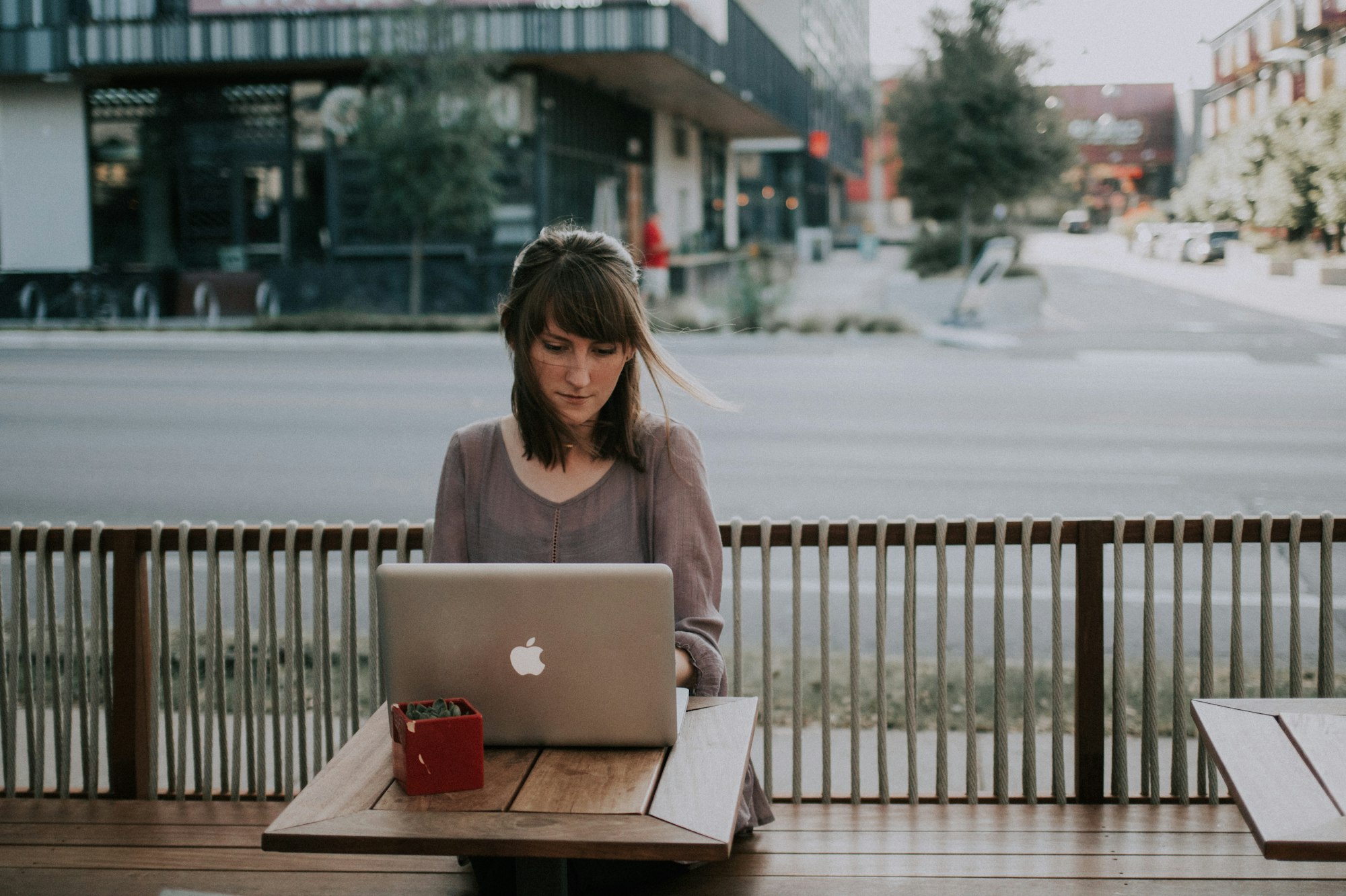 Office Day als Digital Native: Eine Frau sitzt draußen in der Stadt und arbeitet an einem Macbook.