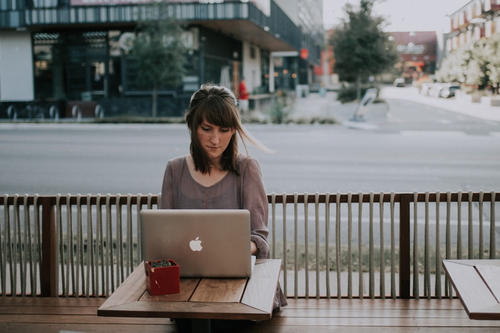 회색 셔츠를 입은 여자가 MacBook 앞 벤치에 앉아 있습니다.