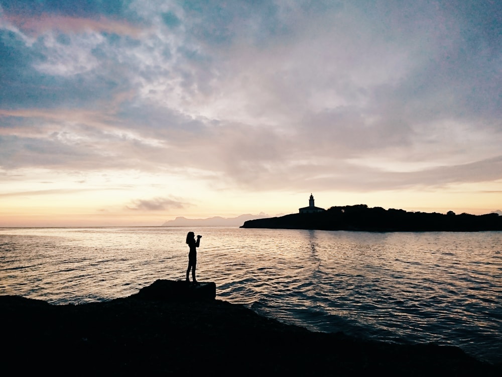 woman standing on rock formation near shoreline