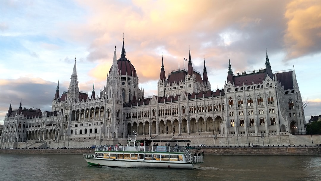 white and brown concrete cathedral building nearby sea, Budapest Parliament seen from a Danube boat cruise on sunset.