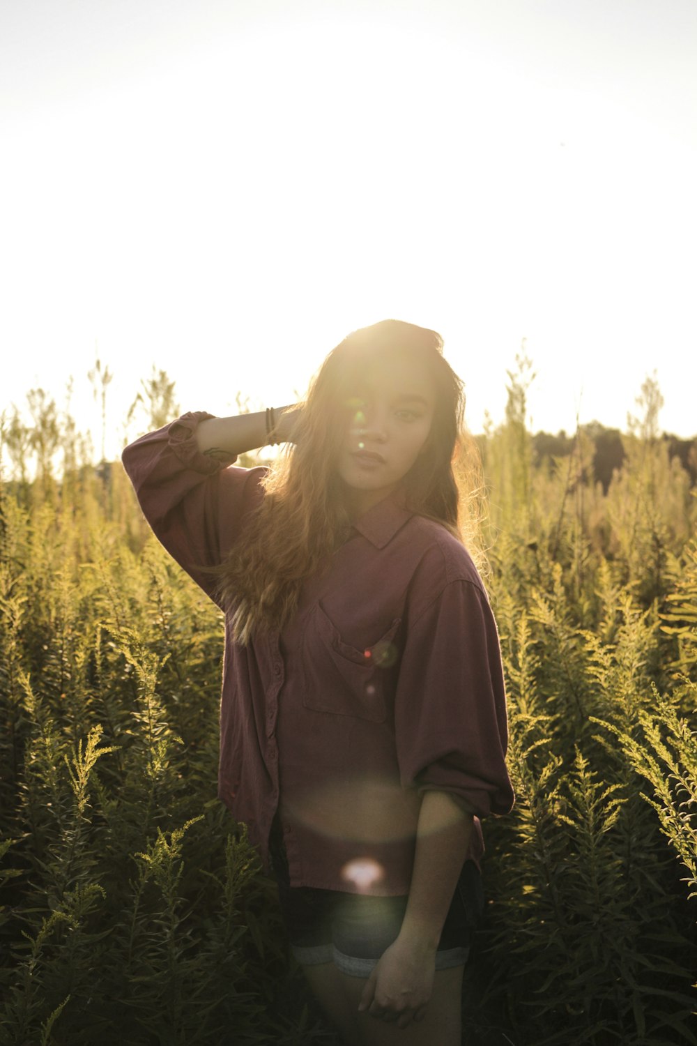 갈색 버튼 업 긴팔 드레스 셔츠를 입고 푸른 잔디 밭 근처에 서 있는 여자