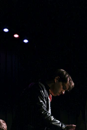 A focused entrepreneur working late in a dark, stylish studio surrounded by premium streetwear items glowing subtly under soft lighting.