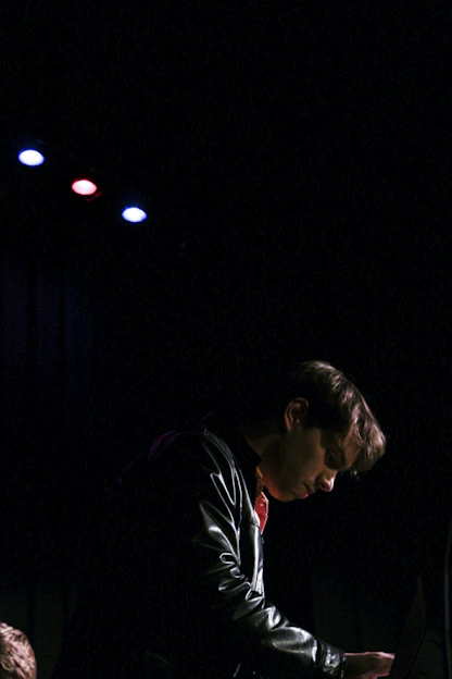 A focused entrepreneur working late in a dark, stylish studio surrounded by premium streetwear items glowing subtly under soft lighting.