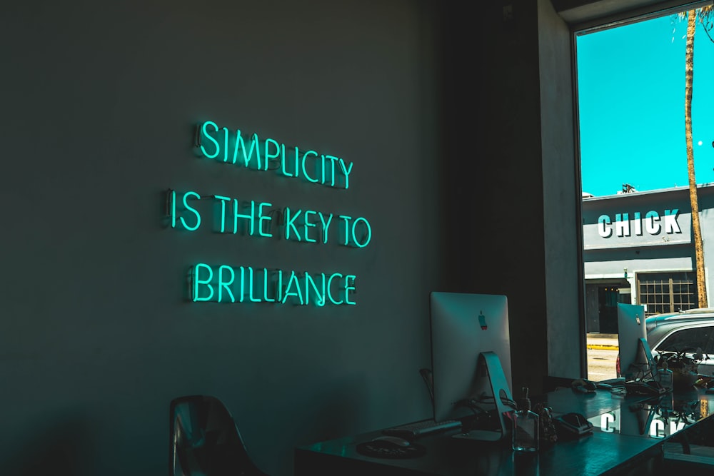 Un cartello luminoso blu su un muro nero che recita "La semplicità è la chiave della brillantezza".