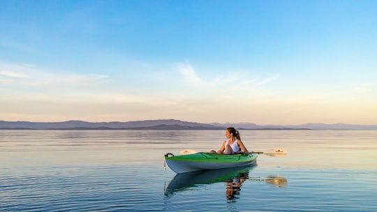 woman on green and white kayak holding yellow oar under white clouds and blue sky in Qualicum Beach Canada