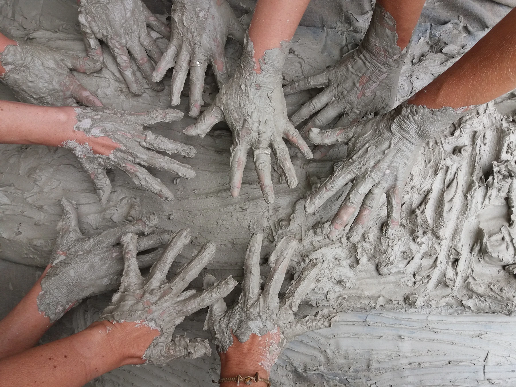 Many pairs of hands pressed into wet gray clay mud