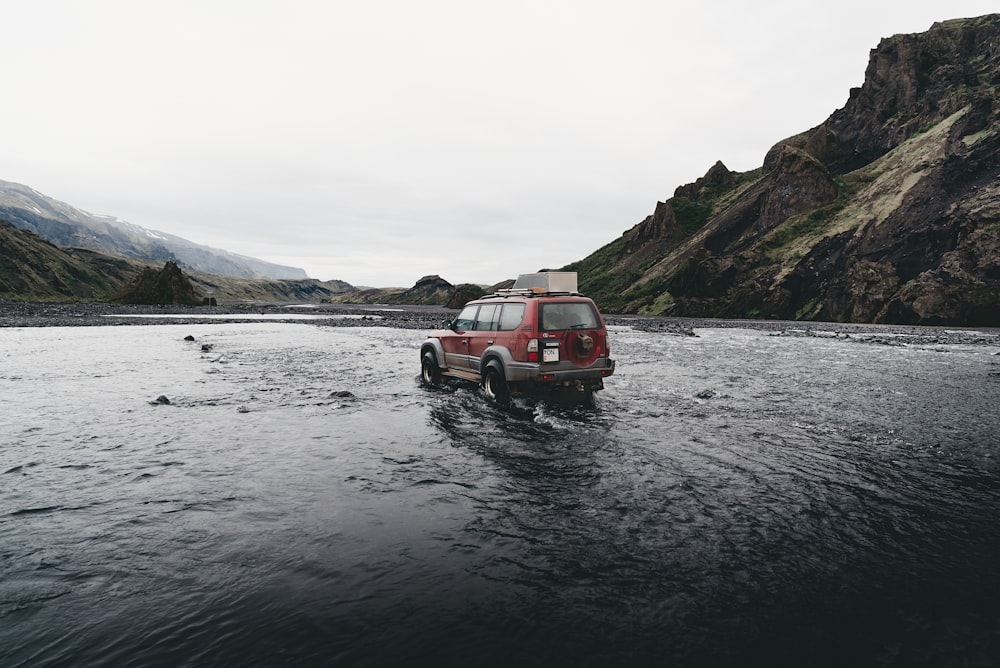 SUV rojo en el agua cerca de la montaña durante el día