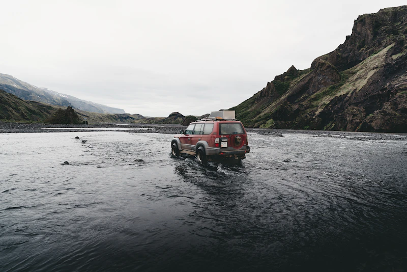 Red SUV near water and mountains