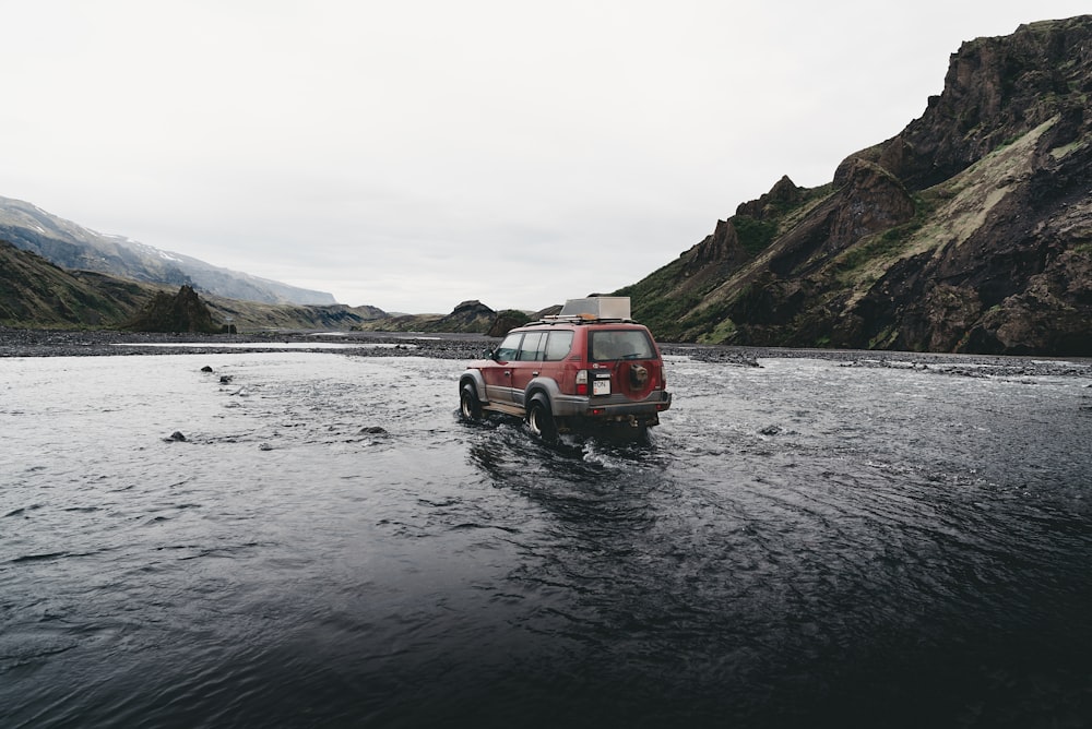 昼間、山の近くの水上を走る赤いSUV