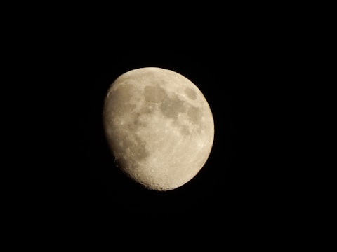 A bright, nearly full moon set against a dark night sky. The surface displays various craters and maria, with clear contrast between the illuminated and shadowed areas.