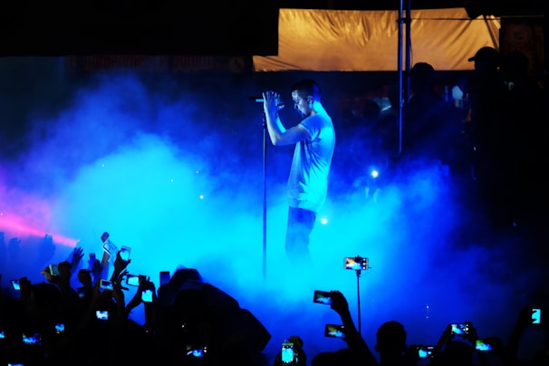 Binaira Mai performing on stage with a deep blue and purple lighting, her voice reaching out to the audience.