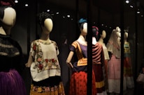 A collection of mannequins adorned with traditional, colorful dresses, featuring elaborate patterns and textiles. Each mannequin has a distinctive hairstyle and pose, creating a sense of cultural heritage and artistic expression.