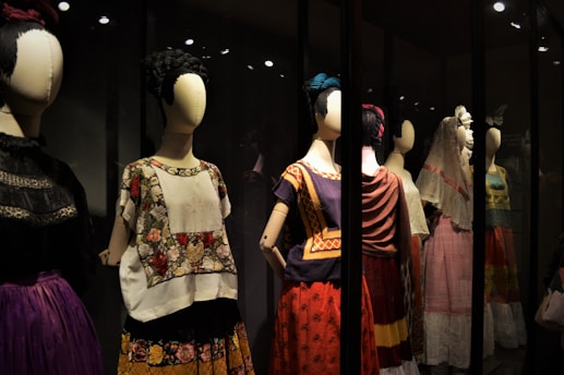 A collection of mannequins adorned with traditional, colorful dresses, featuring elaborate patterns and textiles. Each mannequin has a distinctive hairstyle and pose, creating a sense of cultural heritage and artistic expression.