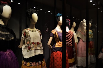 A collection of mannequins adorned with traditional, colorful dresses, featuring elaborate patterns and textiles. Each mannequin has a distinctive hairstyle and pose, creating a sense of cultural heritage and artistic expression.