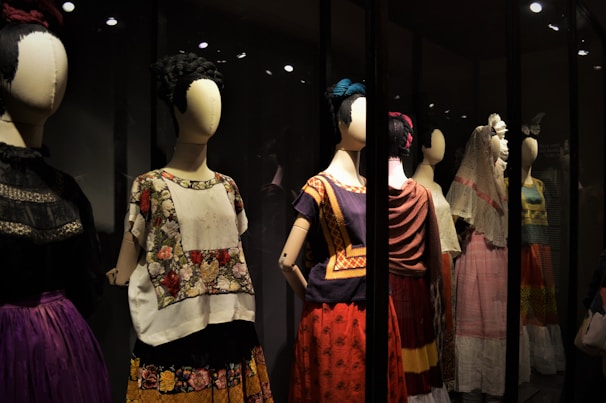 A collection of mannequins adorned with traditional, colorful dresses, featuring elaborate patterns and textiles. Each mannequin has a distinctive hairstyle and pose, creating a sense of cultural heritage and artistic expression.