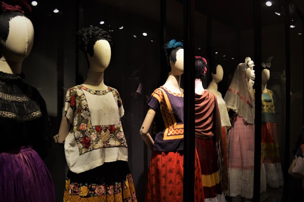 A collection of mannequins adorned with traditional, colorful dresses, featuring elaborate patterns and textiles. Each mannequin has a distinctive hairstyle and pose, creating a sense of cultural heritage and artistic expression.
