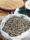 Several bags and containers are filled with different types of corn, including yellow, white, and a black variety. Each type of corn is displayed in a separate bag or container, giving a rich texture and variety to the visual arrangement.