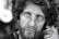The black and white photograph captures the close-up of a middle-aged man with a rugged appearance. His curly hair is disheveled, and he has a thick beard. His eyes stare intently, conveying deep emotion. The skin shows visible signs of weathering and life experience.