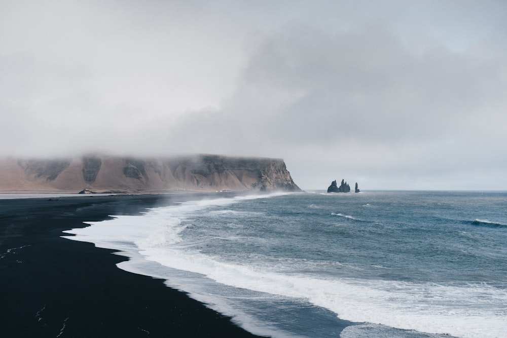 sable noir près du plan d’eau sous le ciel nuageux pendant la journée