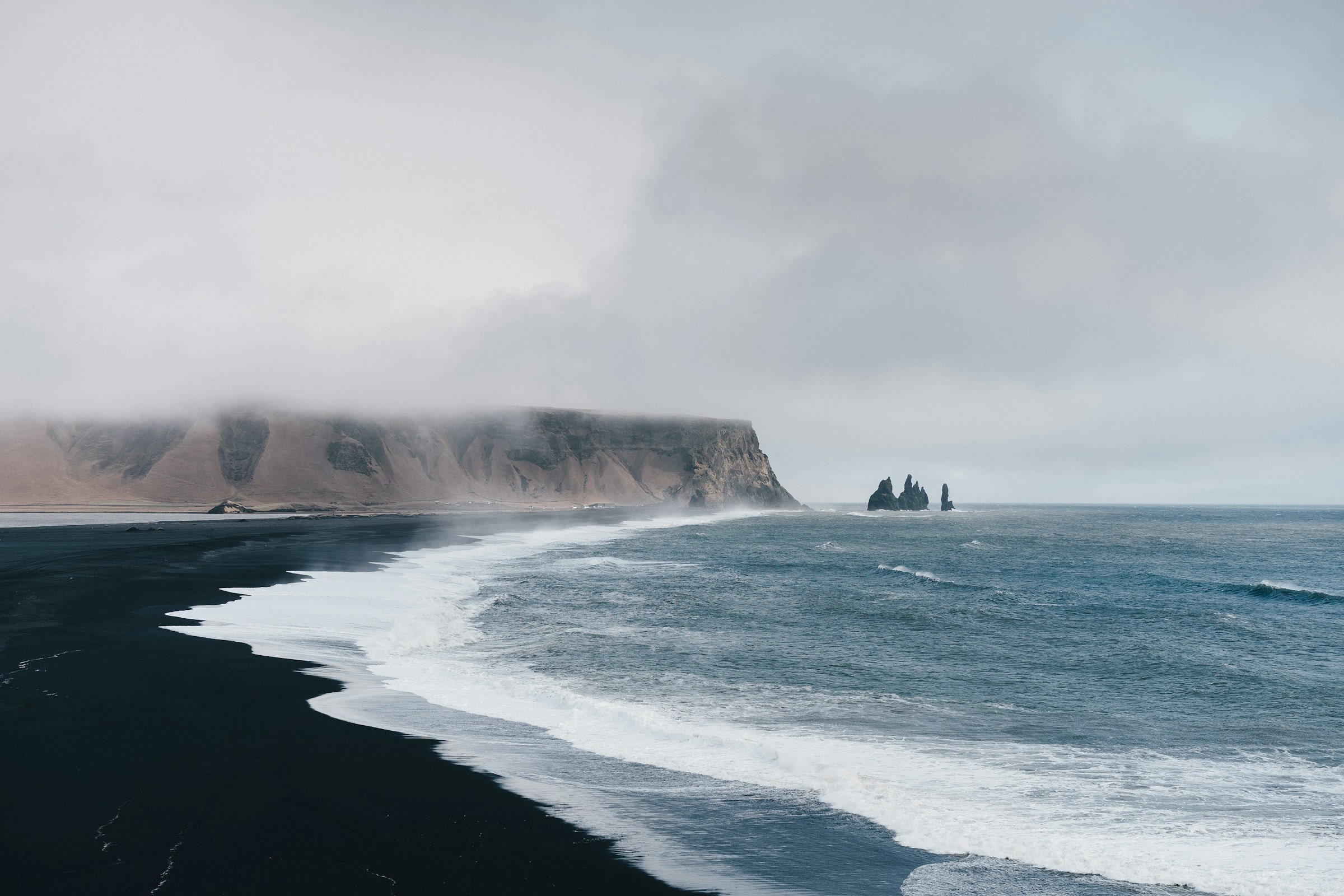 Black sand shore under low cloud, surf running up the beach