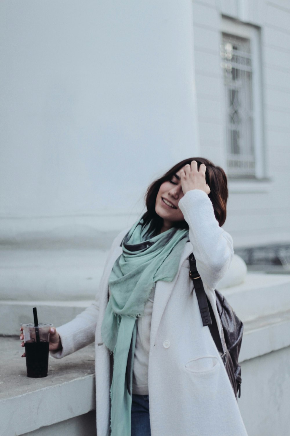 흰색 페인트 건물 근처에서 일회용 컵을 들고 있는 여자