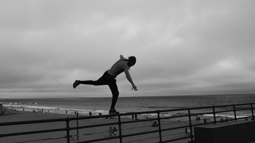 homme debout sur la balustrade en métal surplombant le rivage de la plage sous un ciel nuageux gris pendant la journée