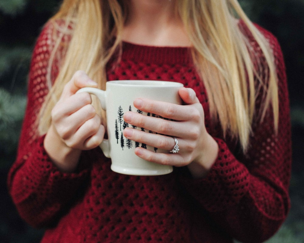 mujer con suéter rojo sosteniendo una taza de cerámica blanca y negra