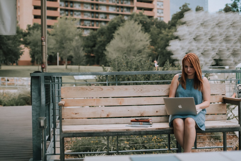 woman sitting on bench white using MacBook Pro