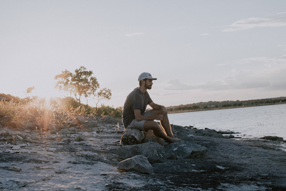 man sitting on rock near body of water during daytime