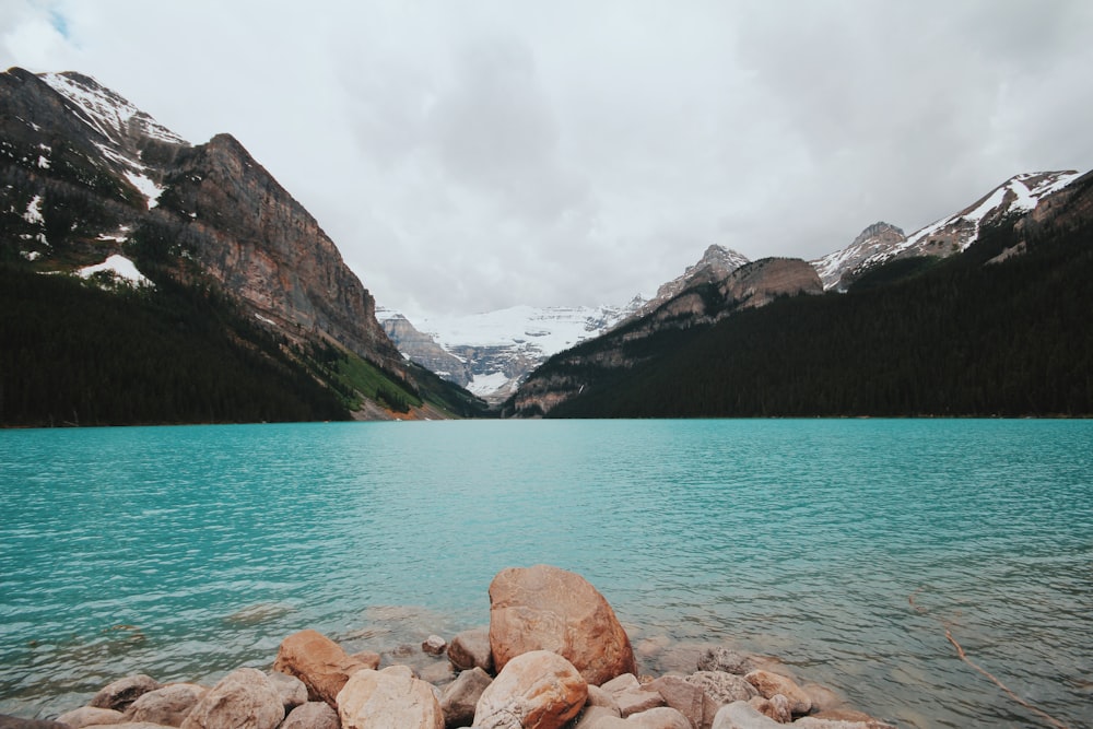 brown rocks beside blue lake near white snowy mountain at daytime