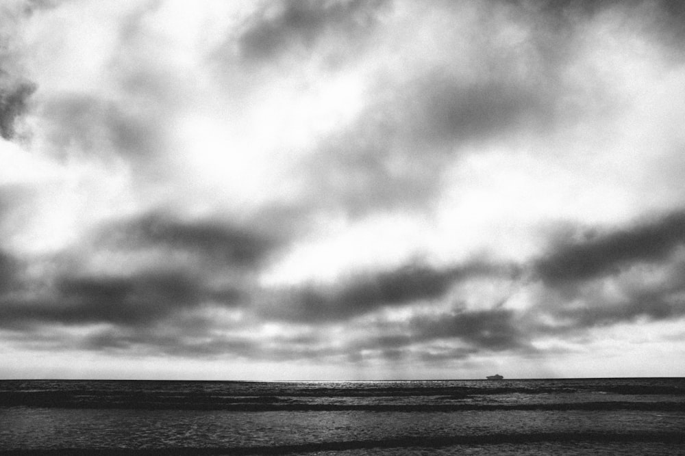 body of water under cloudy sky in grayscale photography